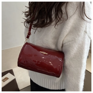 Détail du sac cylindre en cuir verni bordeaux avec plaque dorée et fine bandoulière