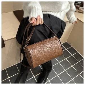 Gros plan du sac bandoulière cylindrique marron foncé avec texture tissée et logo doré