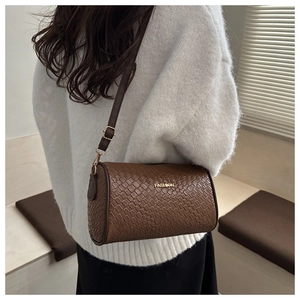 Détail macro du sac cylindrique tressé marron avec plaque métallique dorée FASHION