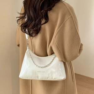 Sac à bandoulière blanc brillant avec chaîne argentée porté sur un manteau beige
