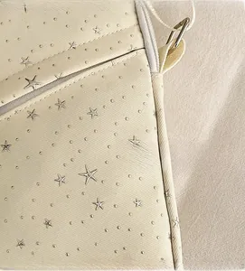 Detail of beige twill crossbody bag featuring silver star rivets and premium texture
