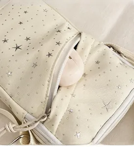 Close-up of the front zipper pocket on a beige crossbody bag with silver star studs