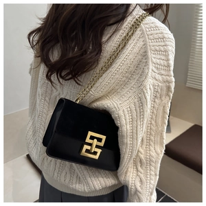 Detail der schwarzen Umhängetasche mit Goldkette und Schloss auf Strickpullover