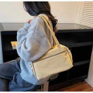 Model wearing a cream nylon rectangular shoulder bag with front zipper and side drawstring