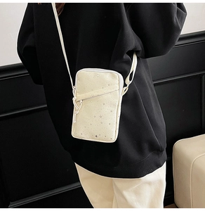 Detail of cream mini crossbody bag with star pattern on black hoodie model