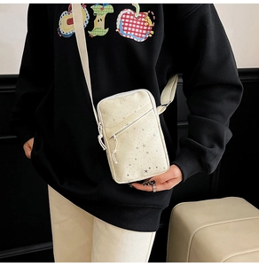 Detail of cream canvas crossbody bag featuring silver star patterns and front zipper pocket