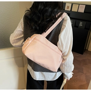 Detailed back view of a light pink nylon crossbody bag worn by a model in a natural setting