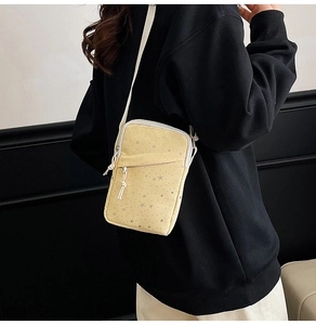 Side view of small yellow canvas crossbody bag with silver star prints on a model