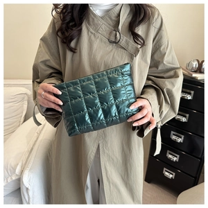 Deep green quilted puffy cosmetic bag held by hand in a stylish minimalist setting