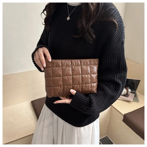 Close-up of brown quilted cotton clutch bag texture held by a model in casual setting