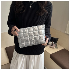 Detail of silver quilted puffer clutch bag held by a model in a modern urban setting