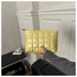Close-up of hand holding a bright yellow quilted cosmetic bag with metallic finish