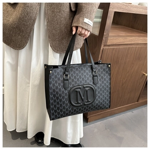 Detail of grey monogram tote bag with embossed M logo and stylish metal rivets