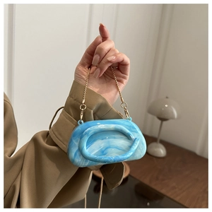 Detail of blue and white marble acrylic clutch bag with elegant golden metal chain strap