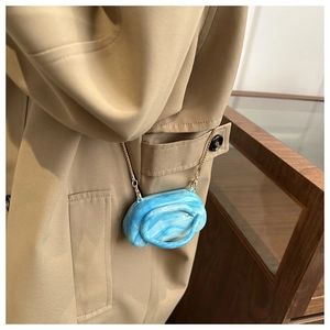 Detail of blue marble acrylic clutch bag with gold chain strap on khaki trench coat