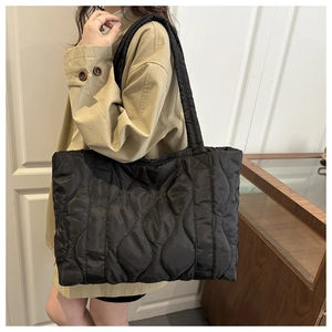 Detail of black quilted tote bag with wave pattern stitching worn with a beige trench coat