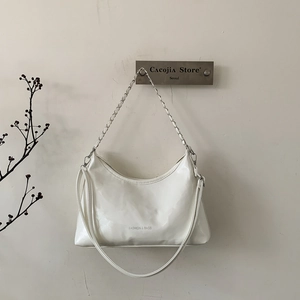 Détail du sac à main en cuir verni blanc avec chaîne argentée et texte gravé