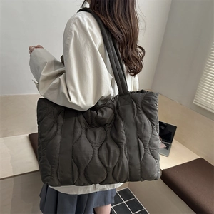 Large dark brown quilted tote bag with wave stitching worn by a model in a minimalist room