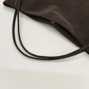 Detail view of the deep brown tote bag showing magnetic closure and slim leather straps