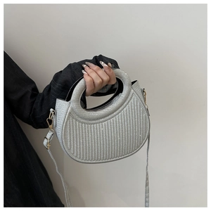 Détail du sac argenté brillant avec texture plissée et poignée ronde évidée