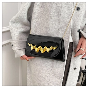 Détail du sac en cuir verni noir avec boucle ondulée dorée et bandoulière chaîne