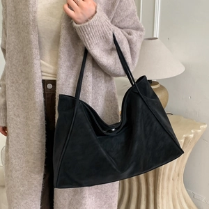 Minimalist large black suede tote bag shown on shoulder in a cozy home setting