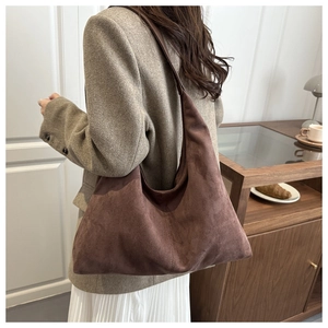 Detail of a brown suede hobo bag shown on shoulder in a minimalist home setting