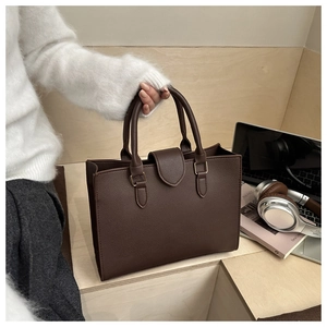 Detail of a deep brown lychee grain leather tote bag with sturdy handles and metal clasp