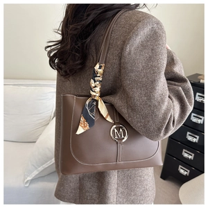Detail of a brown tote bag with metal M buckle and silk scarf on a wool blazer model