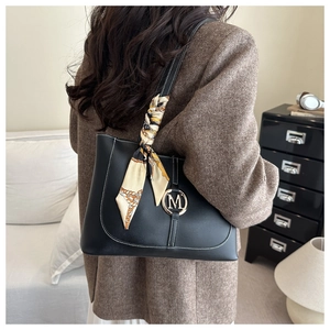Detail of black tote bag with white stitching, gold M logo and silk scarf handle accent