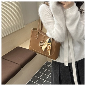 Close-up of brown leather tote bag with silk scarf detail and golden metal M logo