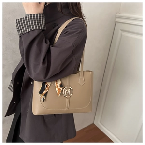 Detail of khaki leather tote bag featuring metal M logo and decorative silk scarf handle