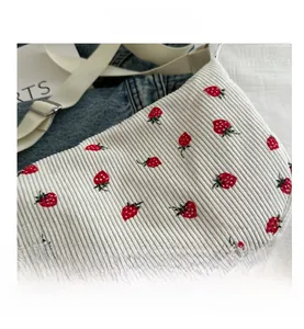 Close-up of strawberry embroidery on off-white corduroy tote bag with adjustable strap