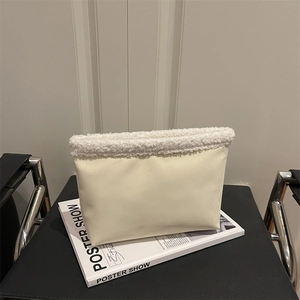 Minimalist beige matte leather shoulder bag with white faux fur trim on a book
