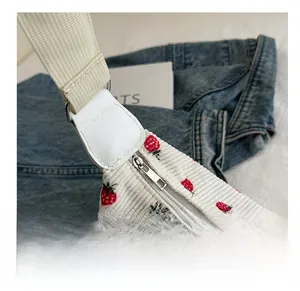 Close-up of smooth metal zipper and woven strap on white corduroy strawberry bag