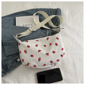 Detail of corduroy crossbody bag featuring a red strawberry print and adjustable strap