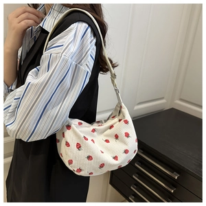 Detail of white corduroy shoulder bag with red strawberry print in a crescent shape