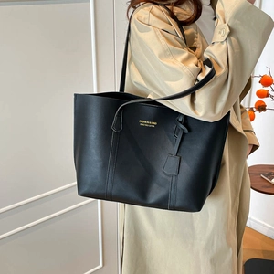 Classic black leather tote bag with gold lettering shown on a model in beige coat