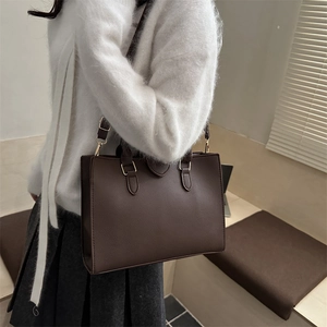 Deep brown leather tote bag with gold buckle on a stylish model with grey pleated skirt