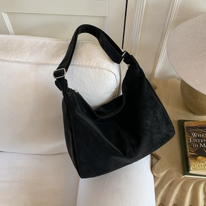 Close-up of black suede hobo bag with adjustable silver buckle on a cozy white sofa