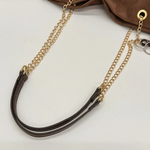 Detailed close-up of golden double chain strap and brown suede fabric on tote bag