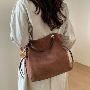 Detail of brown suede tote bag with drawstring, leather handles and cute charm accessory