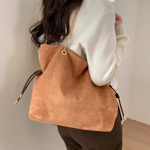 Brown suede slouchy bucket bag with gold chain strap shown on model in home setting
