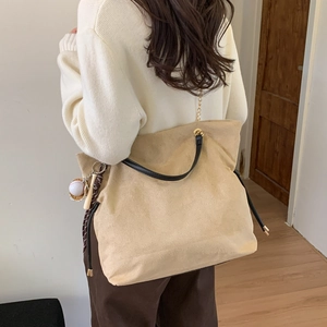 Detail of beige suede bucket bag with black leather handle and baseball charm on a model