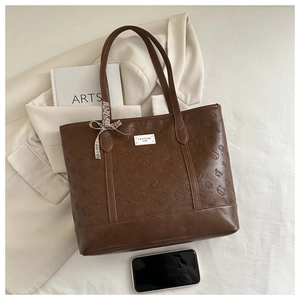 Detail of brown leather tote bag featuring embossed cats and a chic plaid bow decoration