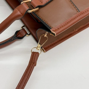 Close-up of golden metal hooks and brown lychee grain leather on a shoulder bag