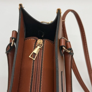 Detail view of brown PU leather handbag featuring a gold zipper and adjustable strap