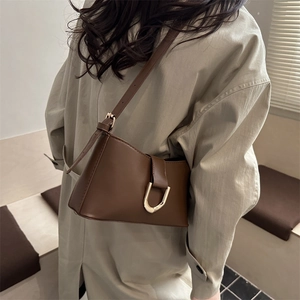 Sac bandoulière minimaliste en cuir marron avec boucle fer à cheval dorée sur manteau