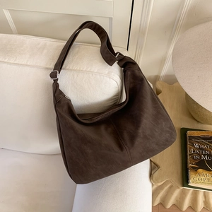 Deep brown matte hobo bag with adjustable wide strap on a white sofa in a cozy interior