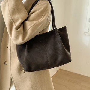 Detail of dark brown leather tote bag with vertical stitching and slim straps on model